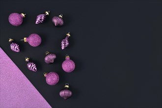 Modern seasonal Christmas flat lay with bright violet glittering tree bauble ornaments on left side and empty dark black copy space on right side