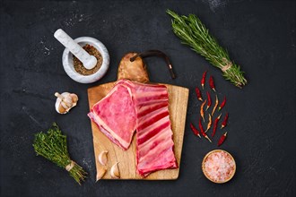Fresh raw lamb breast ribs on wooden cutting board with herbs and seasoning