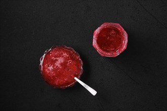 Top view of jar and saucer with cherry jam on black background