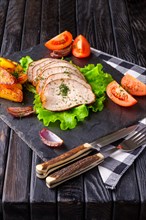 Sliced baked ham with fresh tomatoes on a stone plate in a rustic style