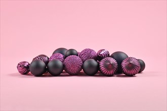 Pile of dark purple and black Christmas tree ornaments in shape of round ball baubles on pink background