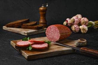 Smoked beef salami and sandwich on cutting board over black background