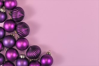 Seasonal dark purple Christmas tree bauble ornaments on side of light pink background with empty copy space