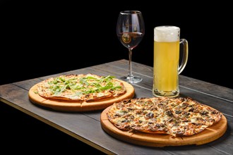 Two pizzas and a glass of lager beer and red wine on a table