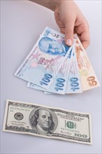 Hands holding Turksh Lira banknotes by the side of American dollar banknotes on white background