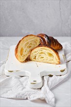 Cross section of classic croissant on bright background and white wooden board