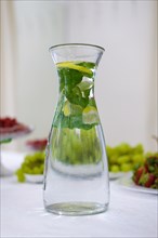 Soft focus photo of decanter with mint and lemon lemonade on table with fruits on bacground