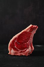Raw rib-eye steak bone in on dark background closeup