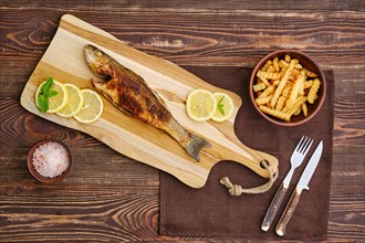 Top view of fried sea bass with fried potato on wooden cutting board
