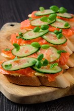 Sandwich with salmon on wooden plate on dark wooden table