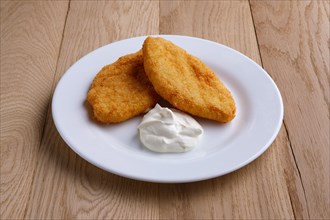 Potato cutlet in breading stuffed with ham served with sour cream on wooden table