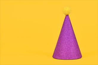 Glittering purple party hat on yellow background with copy space