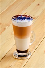 Latte macchiato with chocolate and dry knapweed petals in transparent glass on wooden background