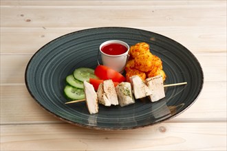 Pieces of chicken fillet on skewer with fried potato balls and vegetables
