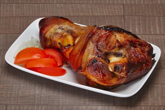 Baked pork shank with fresh slices of onion and tomato on wooden table