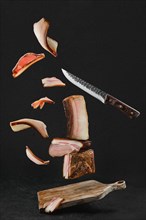 Levitating slices of different smoked pork bacon and lard on wooden cutting board