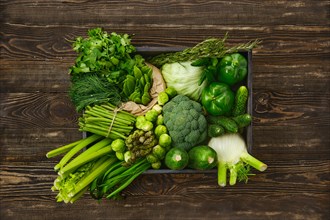 Various fresh green vegetables in wooden box on timber background