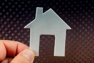 White paper house in hand placed on metal background