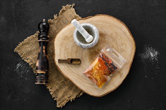 Wooden cross section with a set of spices for pilaf in plastic package and stone mortar and mill