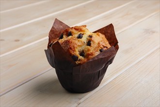 Fresh muffin with chocolate chips in paper wrapper on wooden table