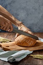 Male hand with knife cutting hot homemade bread