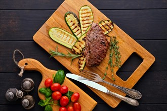 Top view of beef steak and zucchini served with fresh tomato cherry and basil on wooden cutting board