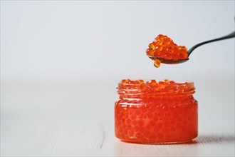 Photo with shallow depth of field of open jar with red caviar and a spoon above it