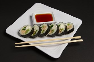 Angle view of portion of chicken teriyaki rolls served on black paper with soy sauce and hashi