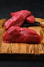 Closeup view of raw beef steak chopped on slices on shabby cutting board