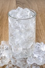 Glass of cold water with ice scattered on wooden table