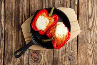 Bell pepper stuffed with meat with melted cheese mozzarella on top baked in oven in cast iron skillet. Top view. Natural wooden background