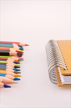 Color pencils of various colors near a notebook on a white background