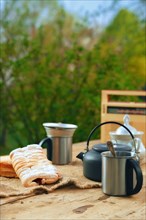 Camping kettle with a mug and biscuit on the table outdoors