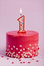 Lighted number one candle red cake with star sprinkles against purple backdrop