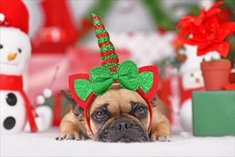 French Bulldog dog with Christmas unicorn headband in front of seasonal decoration