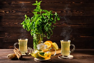 Citrus tea with ginger and mint leaves in a glass teapot on wooden table