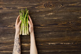 Overhead view of fresh asparagus in hand over wooden background