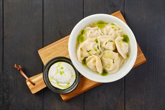 Overhead view of a bowl with pork pelmeni with sour cream on a wooden serving board