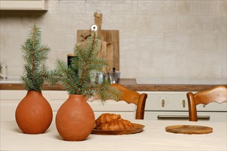 Kitchen table with croissants on plate and two clay vases with fir branches