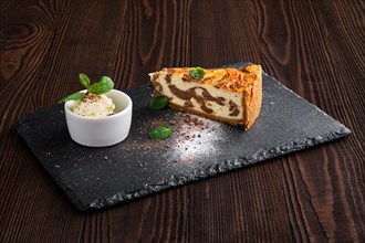 Layered cheesecake with ice cream served on slate plate on dark wooden background