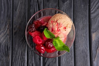 A cup of cherry ice cream decorated with raspberries and dewberry and mint leaves. Top view