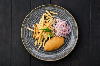 Top view of Kiev cutlet with american fries and red cabbage with carrot as a garnish