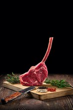 Raw juicy cowboy steak on wooden cutting board with spice