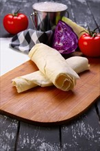 Rolled pita with fresh vegetables on wooden board with a napkin on a table