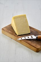 Triangular piece of hard cheese on wooden cutting board