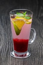 Tall transparent glass with raspberry and citrus tea on dark wooden table