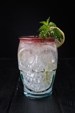 Variation of gin and tonic cocktail with cherry syrup in skull cup on dark wooden background