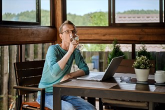 Middle aged man drinking wine while chatting in messenger on laptop