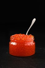 Open jar with red caviar and a spoon in it