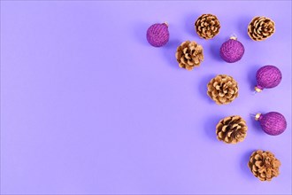 Seasonal Christmas flat lay with fir cones and glittering tree baubles on right side and empty purple copy space on left side on light purple background